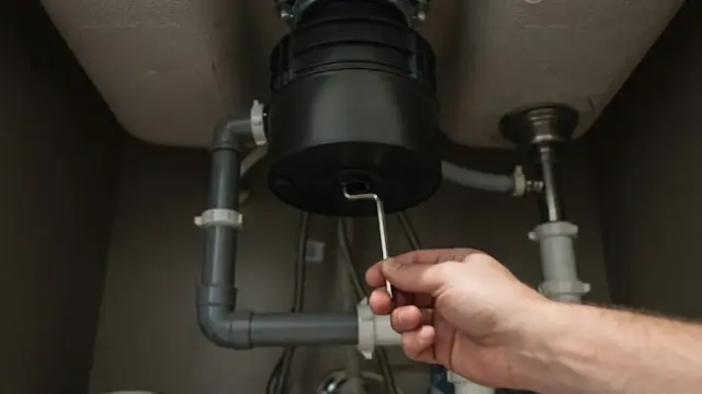 Hand turning a hex key in the bottom of a garbage disposal under a sink to free a jam