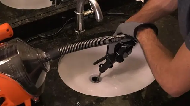 Gloved hands feeding a drain machine cable into a bathroom sink drain