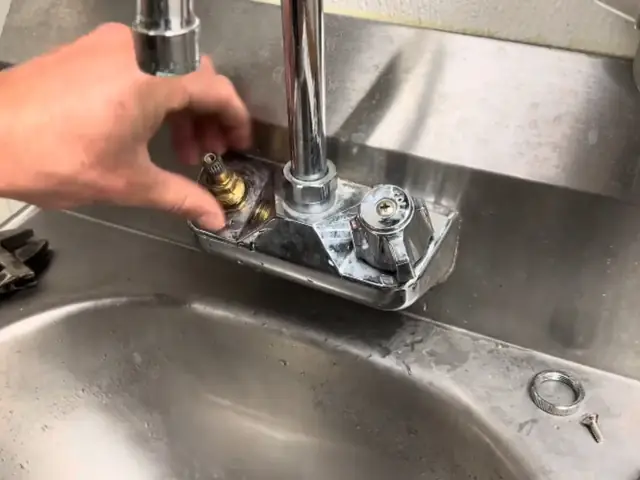 Hands removing the handle cartridge from a chrome faucet on a stainless steel sink